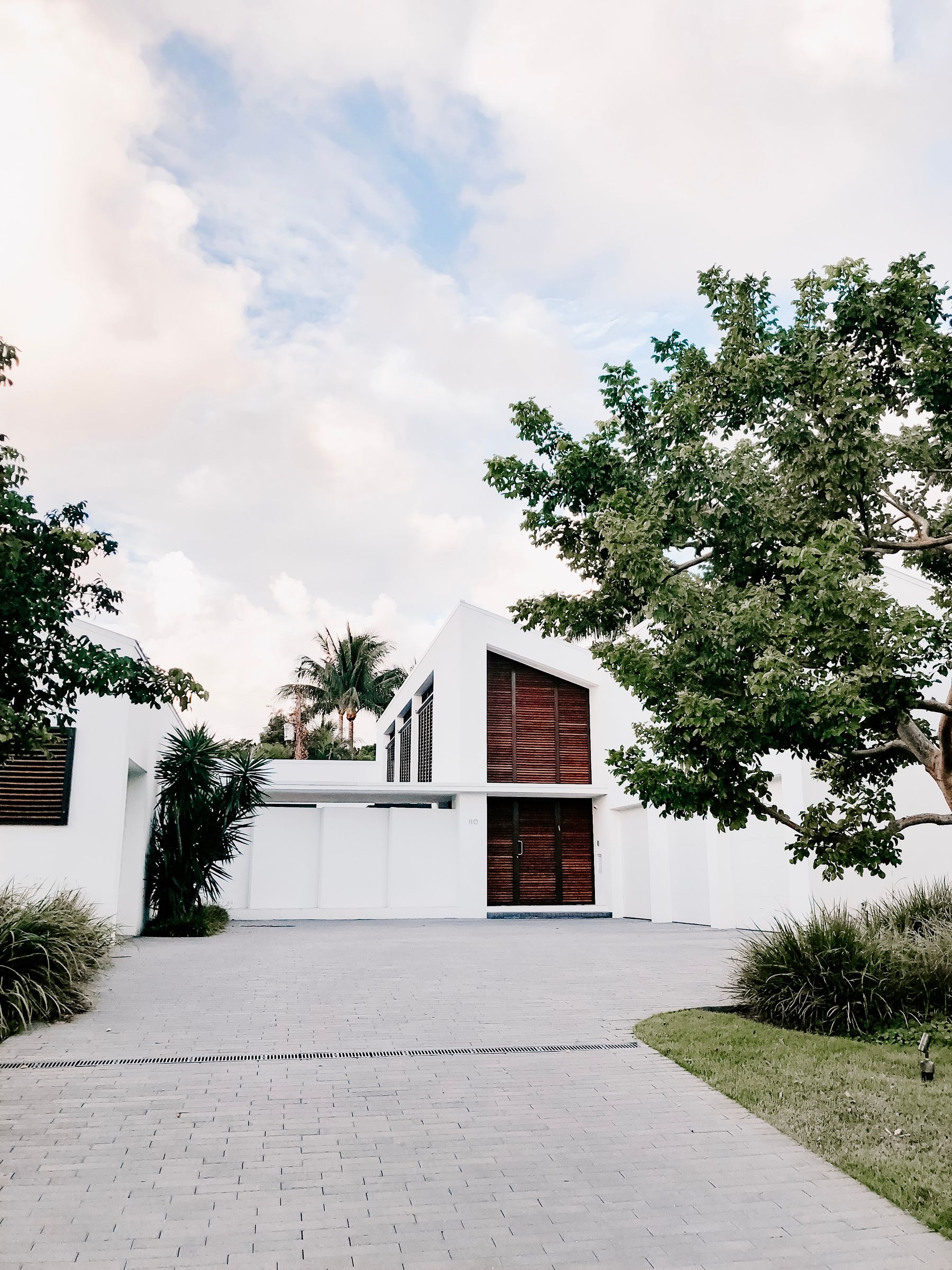 White modern home with a dark wood entry under large trees