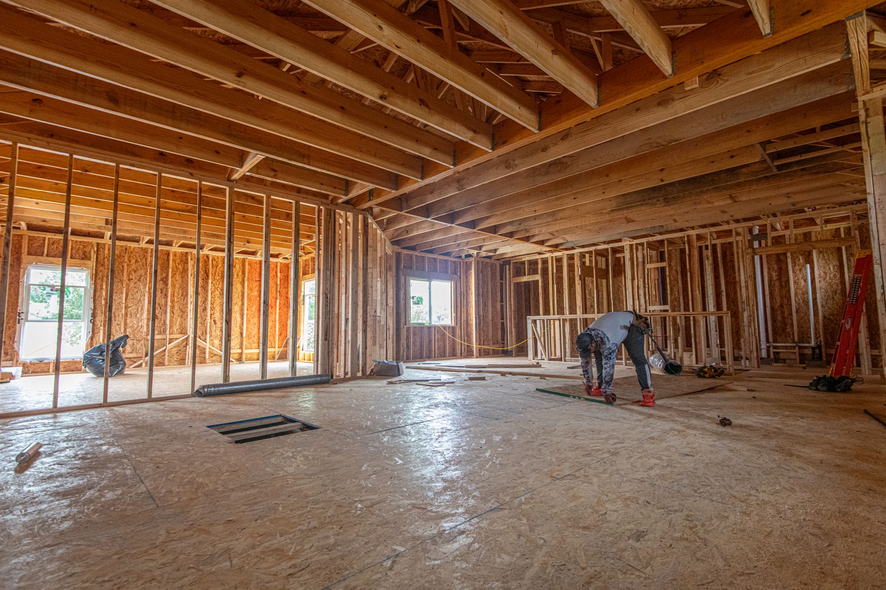 Interior of a house under construction with fresh framing and a worker in the background